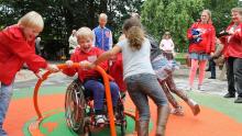 Kinderen spelen samen in een speeltuin. Een van de kinderen zit in een rolstoel.